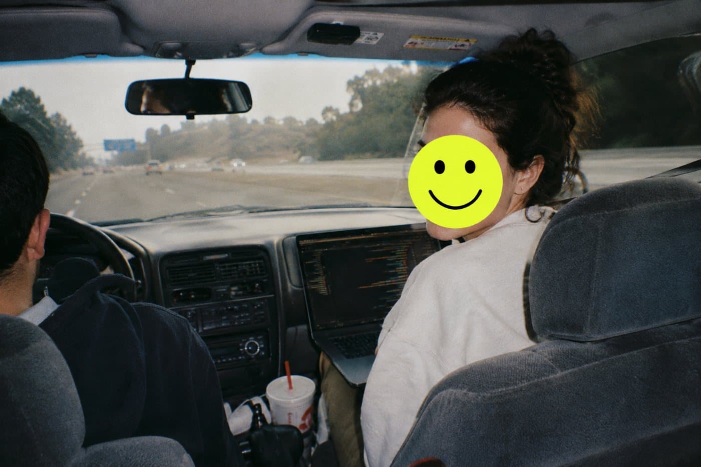 A founder coding on a laptop in the passenger seat on a road trip